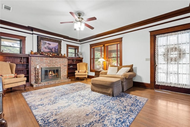 living room featuring ceiling fan, a fireplace, crown molding, and light wood-type flooring