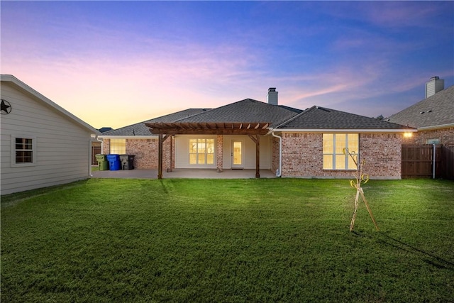 back house at dusk with a pergola, a patio area, and a lawn