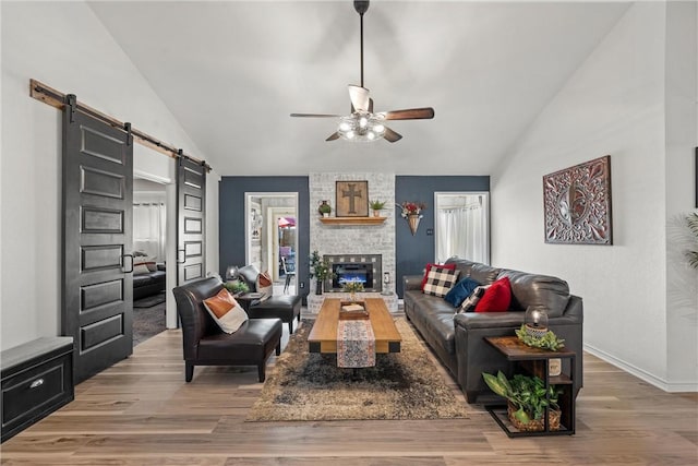 living room with a barn door, ceiling fan, lofted ceiling, and light wood-type flooring