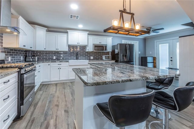 kitchen featuring white cabinetry, sink, wall chimney exhaust hood, stainless steel appliances, and a kitchen island