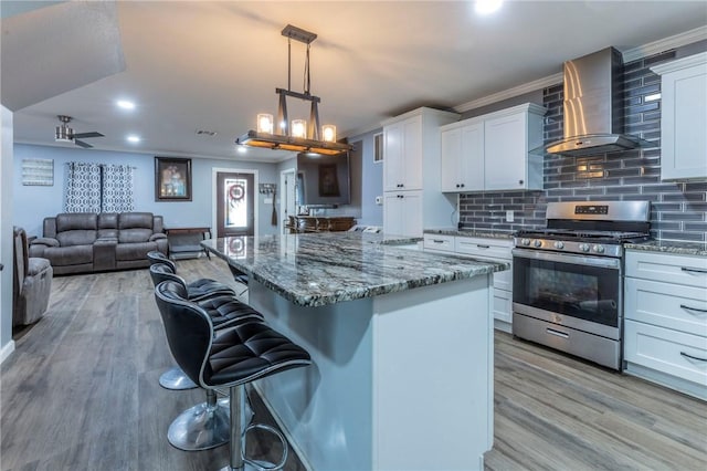 kitchen with white cabinetry, wall chimney exhaust hood, stainless steel gas range oven, a kitchen bar, and decorative backsplash