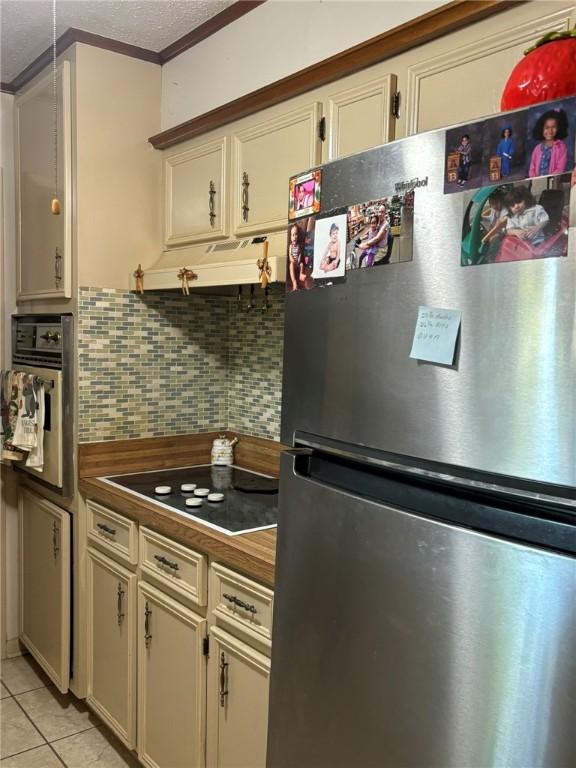 kitchen with crown molding, a textured ceiling, light tile patterned floors, appliances with stainless steel finishes, and backsplash