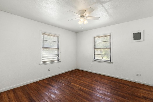 empty room with a textured ceiling, ceiling fan, dark wood-type flooring, and a wealth of natural light