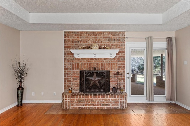 unfurnished living room featuring hardwood / wood-style flooring, a textured ceiling, and a brick fireplace