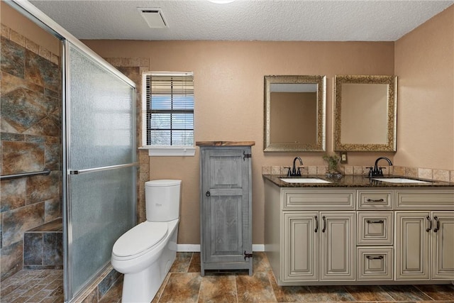 bathroom with a shower with door, vanity, a textured ceiling, and toilet