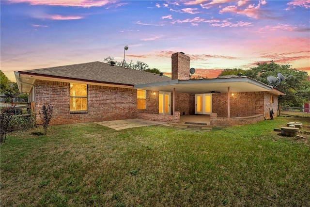 back house at dusk featuring a patio, ceiling fan, and a lawn