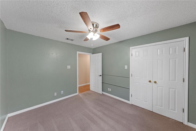 unfurnished bedroom featuring a closet, a textured ceiling, light colored carpet, and ceiling fan