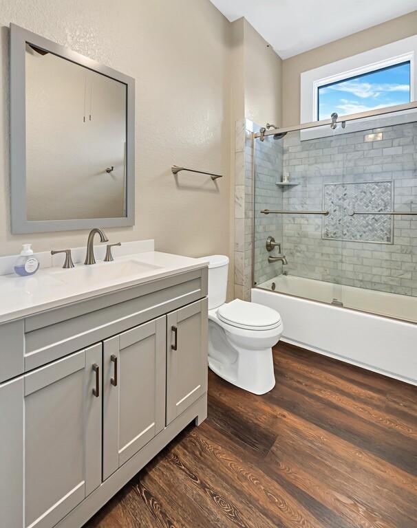 full bathroom featuring toilet, vanity, bath / shower combo with glass door, and hardwood / wood-style flooring