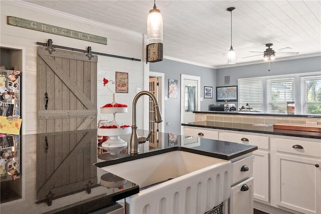 kitchen with ceiling fan, sink, pendant lighting, a barn door, and white cabinetry