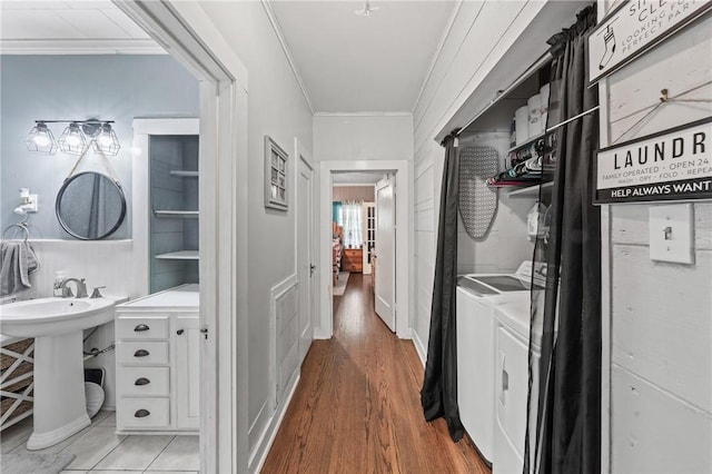 laundry area with sink, wood-type flooring, ornamental molding, and washing machine and clothes dryer