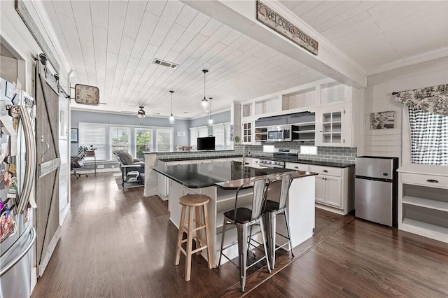 kitchen featuring hanging light fixtures, a barn door, a breakfast bar area, white cabinets, and appliances with stainless steel finishes