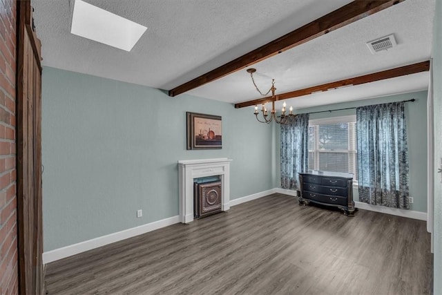 unfurnished living room featuring beamed ceiling, wood finished floors, visible vents, and a textured ceiling