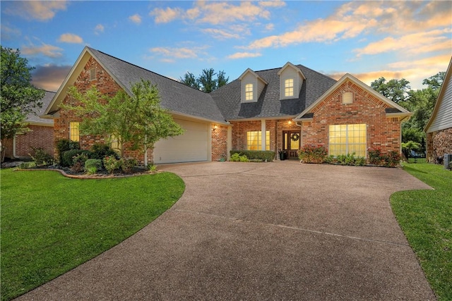 view of front of home featuring brick siding, roof with shingles, an attached garage, a front yard, and driveway