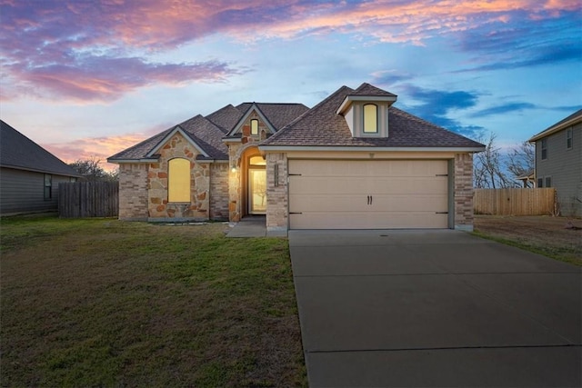 french country home with an attached garage, fence, concrete driveway, and a front yard