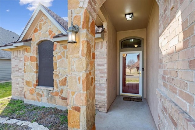 entrance to property featuring stone siding, a shingled roof, and brick siding