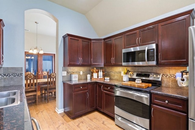 kitchen featuring light wood-type flooring, appliances with stainless steel finishes, decorative backsplash, and lofted ceiling