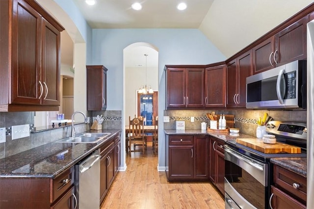 kitchen featuring light wood finished floors, dark stone countertops, a sink, stainless steel appliances, and a notable chandelier