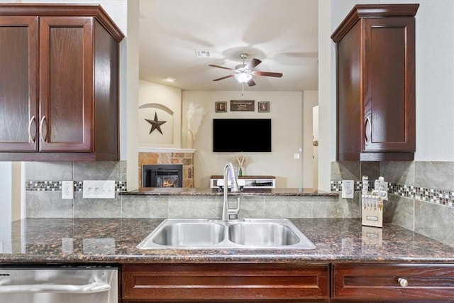 kitchen with dishwasher, a tile fireplace, backsplash, open floor plan, and a sink