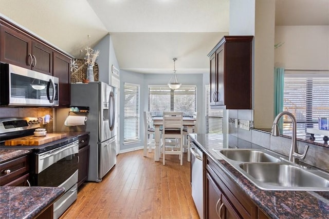 kitchen with light wood finished floors, stainless steel appliances, lofted ceiling, tasteful backsplash, and a sink