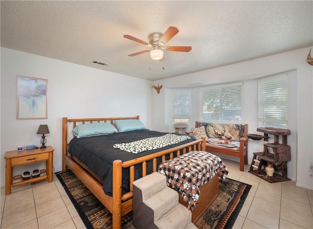 bedroom featuring ceiling fan, light tile patterned floors, and a textured ceiling