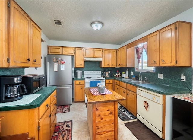 kitchen with sink, stainless steel appliances, a kitchen island, a textured ceiling, and light tile patterned flooring