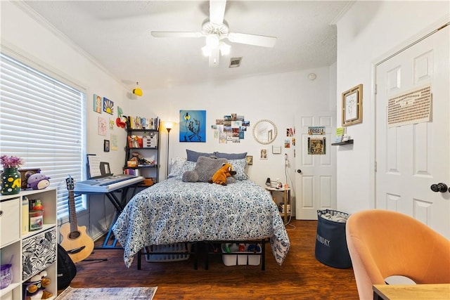 bedroom with ceiling fan, dark wood-type flooring, ornamental molding, and visible vents