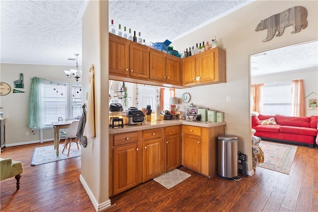 kitchen featuring brown cabinetry, dark wood finished floors, light countertops, a textured ceiling, and a notable chandelier