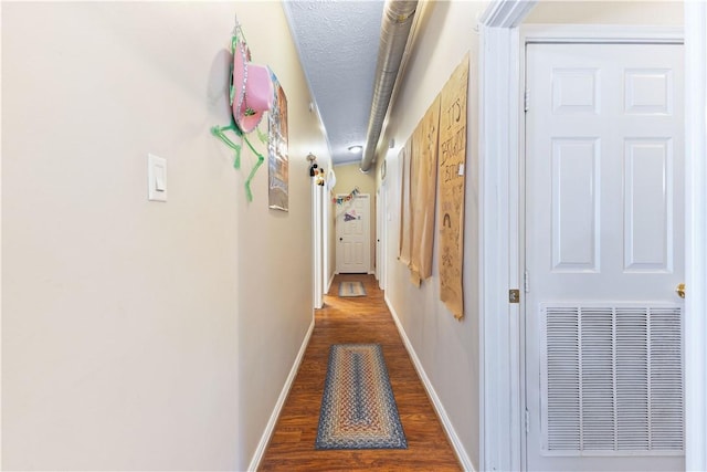 corridor featuring visible vents, a textured ceiling, baseboards, and dark wood-type flooring