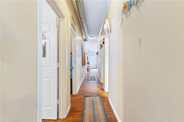 hallway featuring a textured ceiling, baseboards, and wood finished floors