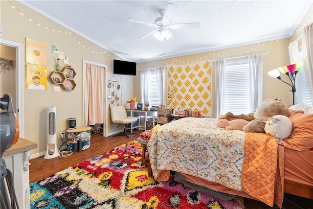 bedroom featuring a textured ceiling, wood finished floors, a ceiling fan, baseboards, and crown molding