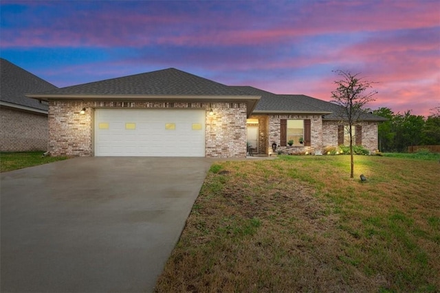 view of front of house featuring an attached garage, a shingled roof, brick siding, driveway, and a lawn