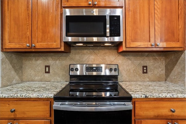 kitchen with light stone counters, brown cabinets, tasteful backsplash, stainless steel microwave, and electric range