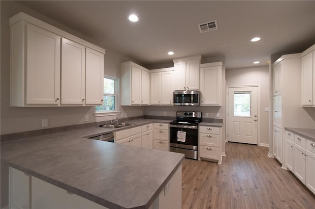 kitchen featuring kitchen peninsula, a wealth of natural light, sink, stainless steel appliances, and white cabinets