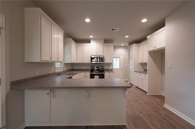 kitchen with a wealth of natural light, white cabinets, stainless steel appliances, kitchen peninsula, and a breakfast bar