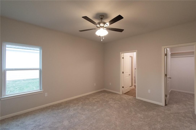 unfurnished bedroom featuring ensuite bathroom, ceiling fan, a closet, light colored carpet, and a walk in closet