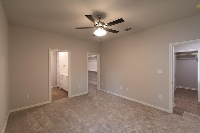 unfurnished bedroom featuring ensuite bath, a walk in closet, ceiling fan, and light colored carpet