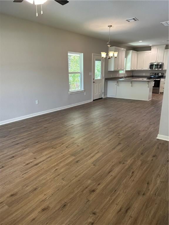 unfurnished living room featuring dark wood-type flooring and ceiling fan with notable chandelier