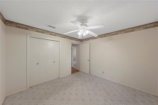 unfurnished bedroom featuring ceiling fan, a closet, light colored carpet, and a textured ceiling