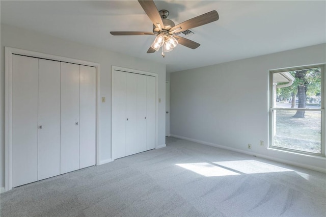 unfurnished bedroom featuring ceiling fan, light carpet, and two closets