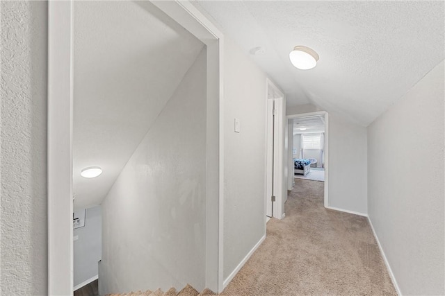 hallway with vaulted ceiling, light colored carpet, and a textured ceiling