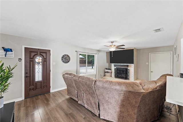 living room featuring dark wood-type flooring, ceiling fan, and a brick fireplace