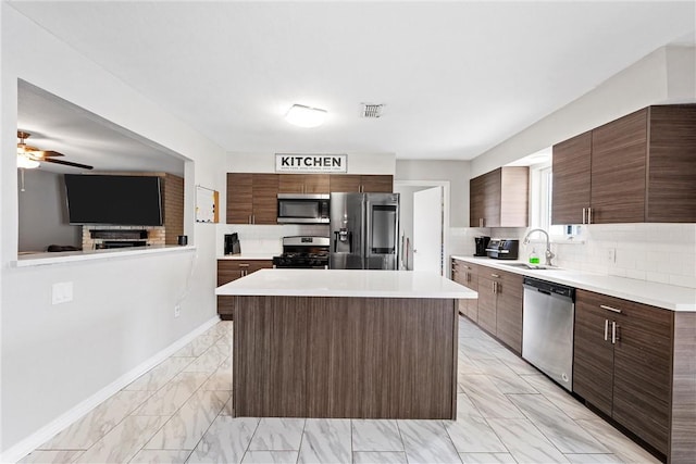 kitchen with sink, appliances with stainless steel finishes, dark brown cabinets, a center island, and tasteful backsplash