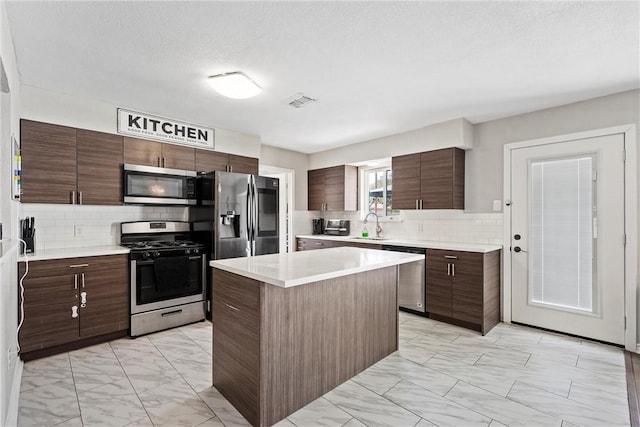 kitchen with appliances with stainless steel finishes, a center island, dark brown cabinetry, tasteful backsplash, and a textured ceiling