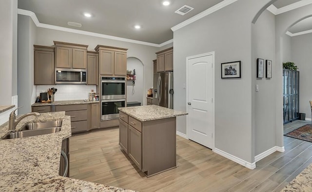 kitchen with sink, stainless steel appliances, light stone counters, light hardwood / wood-style floors, and a kitchen island