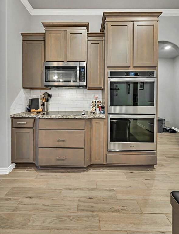 kitchen featuring backsplash, light stone countertops, ornamental molding, and appliances with stainless steel finishes