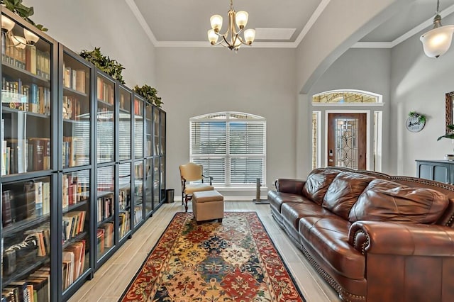 living room with crown molding, a towering ceiling, light hardwood / wood-style floors, and a notable chandelier