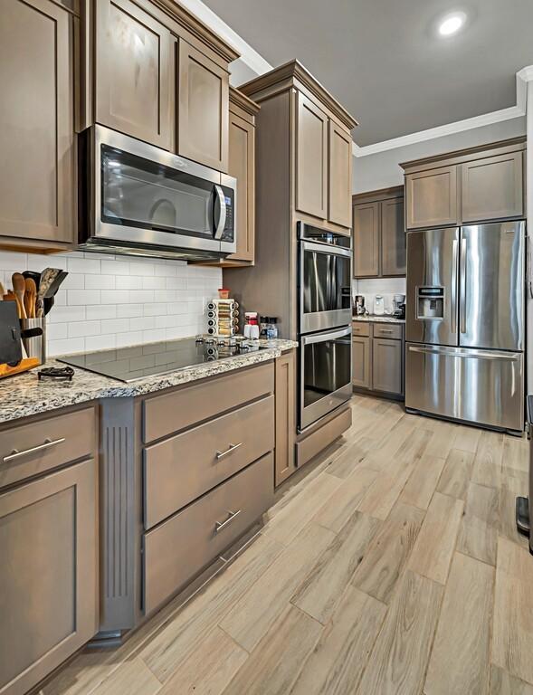 kitchen featuring stainless steel appliances, light stone counters, light hardwood / wood-style flooring, backsplash, and crown molding