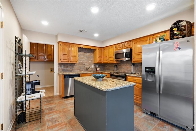 kitchen with a kitchen island, decorative backsplash, stainless steel appliances, light stone countertops, and a textured ceiling