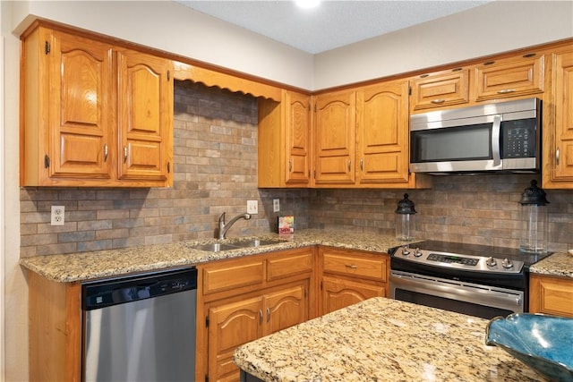 kitchen with stainless steel appliances, sink, light stone counters, and decorative backsplash