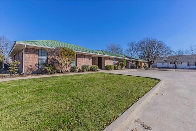 ranch-style home with driveway, a standing seam roof, a front lawn, brick siding, and metal roof